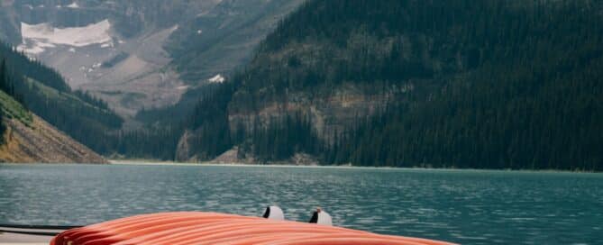 Red canoes are stacked near a mountain lake.